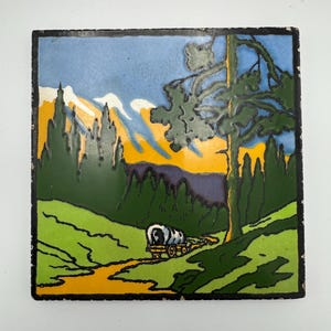 May include: Square ceramic tile depicting a landscape scene with a covered wagon, trees, and mountains. The tile has a black border and a colour palette of green, blue, yellow, and white. The artwork depicts a sunny day with a clear sky.