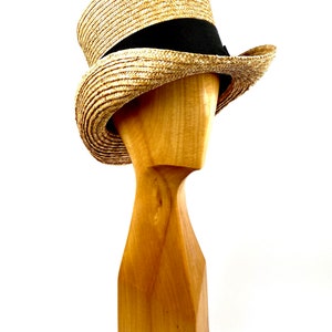 May include: A straw boater hat with a black ribbon band. The hat is on a wooden hat stand.