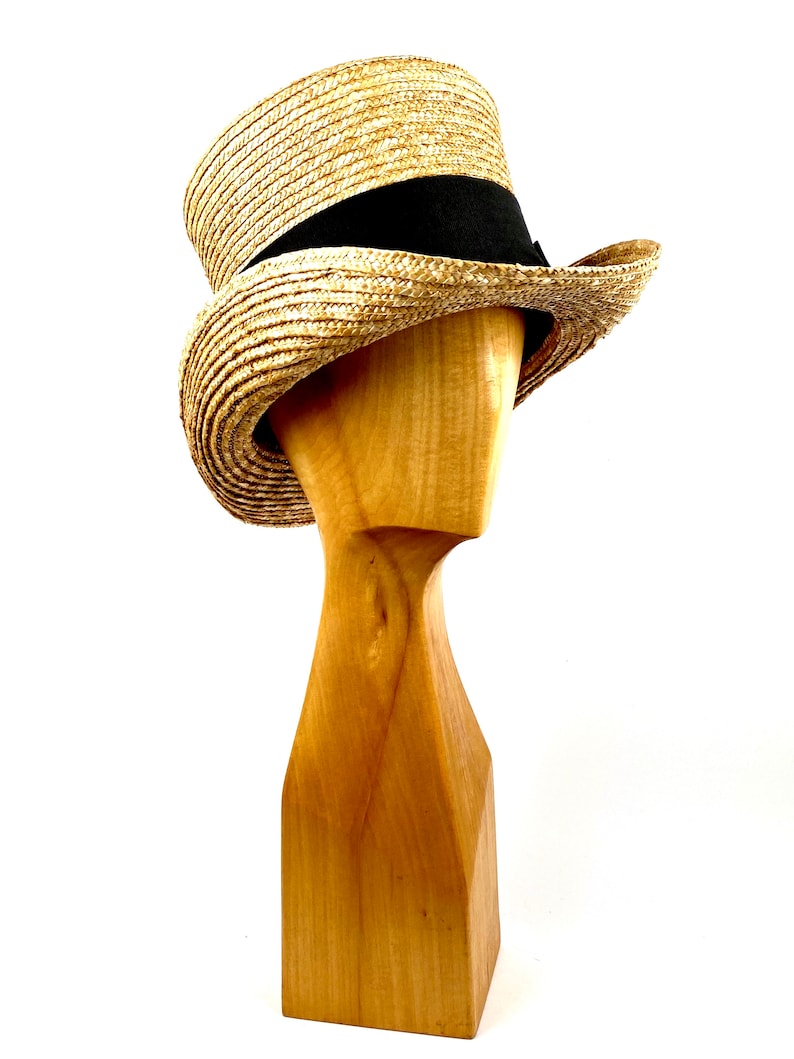 May include: A straw boater hat with a black ribbon band. The hat is on a wooden hat stand.