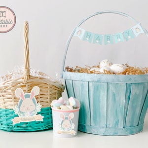 May include: Two Easter baskets, one blue and one wicker, with bunny decorations and the name "Harrison" on the smaller basket. The blue basket has a banner that says "HARRY" and is filled with brown shredded paper and white eggs.