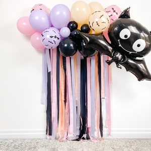 Peut inclure: Une toile de fond de f&ecirc;te d'Halloween avec un ballon de chauve-souris noir, des ballons noirs, violets et roses, et un rideau de rubans roses, violets et noirs.