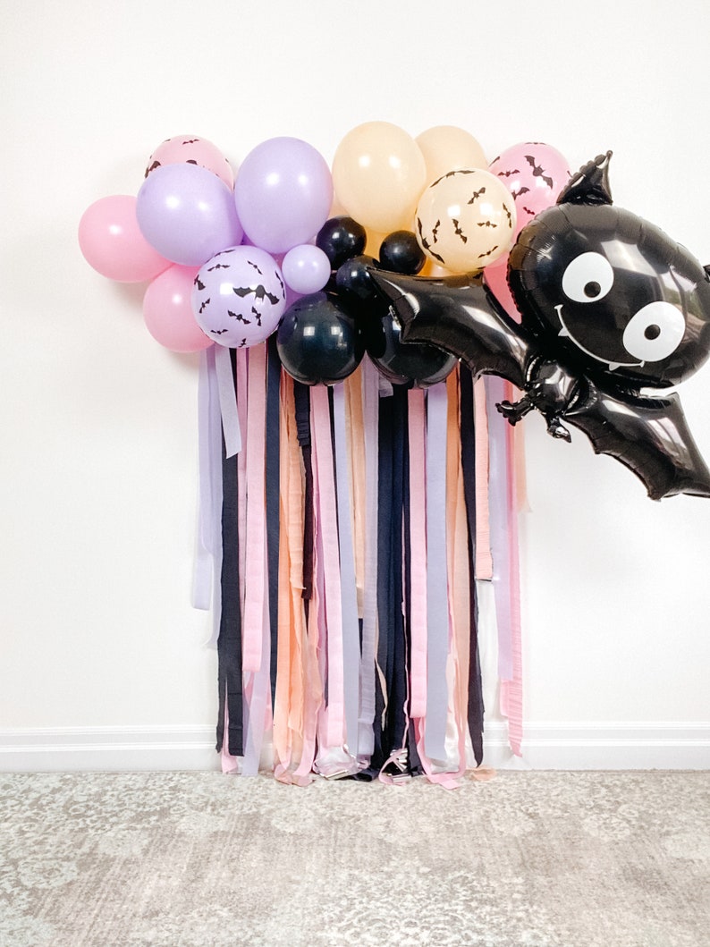 Peut inclure: Une toile de fond de f&ecirc;te d'Halloween avec un ballon de chauve-souris noir, des ballons noirs, violets et roses, et un rideau de rubans roses, violets et noirs.
