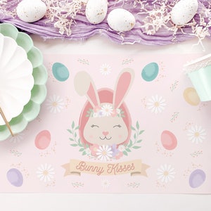 May include: Pink bunny rabbit with a floral crown and the text "Bunny Kisses" on a pink placemat with a white background and pastel colored eggs.