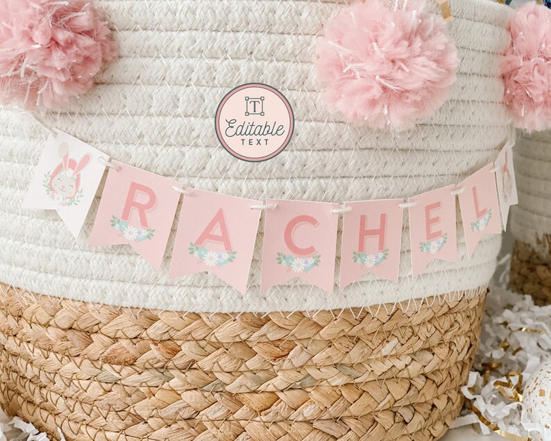 May include: A pink and white banner with the name "RACHEL" in pink letters. The banner is decorated with small flowers and is hanging from a woven basket.
