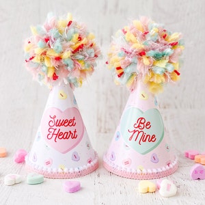 May include: Two pink and white party hats with colorful yarn pom-poms on top. One hat says "Sweet Heart" in red letters on a pink heart and the other says "Be Mine" in red letters on a green heart.