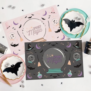 Op de afbeelding: Twee roze en zwarte Halloween-placemats met een griezelig magisch kristallen bol-ontwerp. De placemats bevatten vleermuizen, sterren en een heksenhoed. De tekst "Spooky Magic" is op de placemats gedrukt.