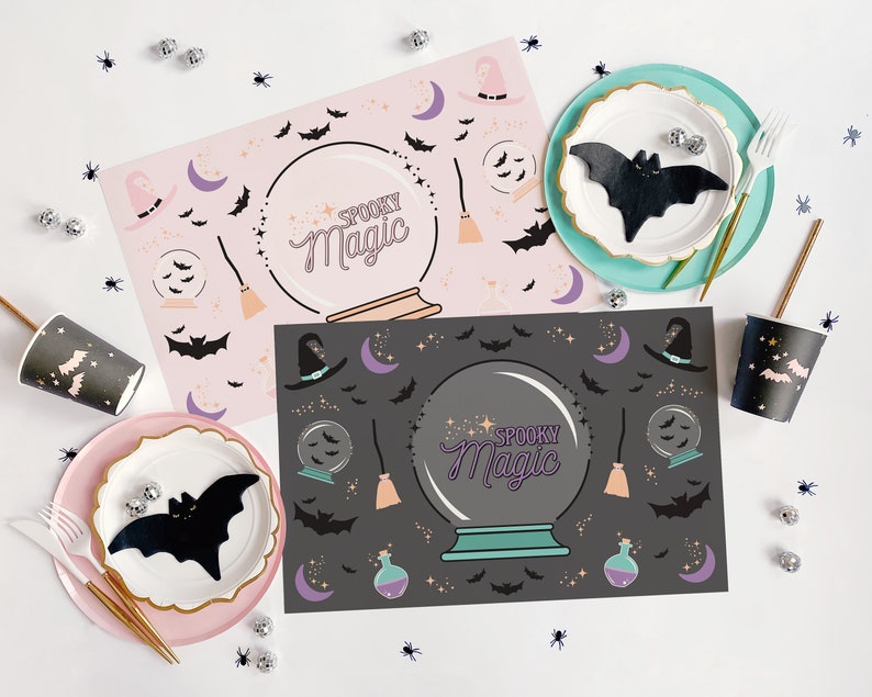 Op de afbeelding: Twee roze en zwarte Halloween-placemats met een griezelig magisch kristallen bol-ontwerp. De placemats bevatten vleermuizen, sterren en een heksenhoed. De tekst "Spooky Magic" is op de placemats gedrukt.