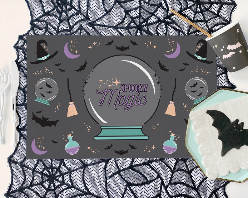 Op de afbeelding: Een zwart-wit Halloween-placemat met een griezelige magische kristallen bol, vleermuizen, sterren, manen, heksenhoeden en bezems. De tekst "Spooky Magic" staat in paars op de kristallen bol.