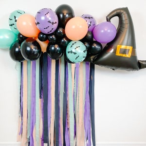 May include: A Halloween party decoration featuring a black witch hat balloon, purple, green, and orange balloons, and black and purple streamers.