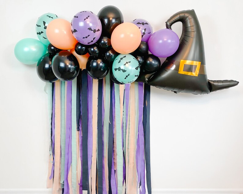 May include: A Halloween party decoration featuring a black witch hat balloon, purple, green, and orange balloons, and black and purple streamers.