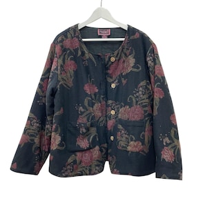 May include: A black jacket with a floral pattern in shades of burgundy, green, and tan. The jacket has a round neckline, wooden buttons, and two front pockets. The jacket is hanging on a white hanger.