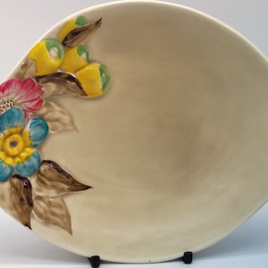 May include: A cream-coloured ceramic serving dish with a floral design. The dish features a raised design of pink, blue, and yellow flowers with brown leaves and yellow berries.