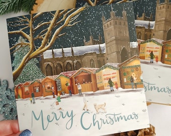 May include: A Christmas card featuring a snowy night scene with a church, a Christmas market, and the text "Merry Christmas".