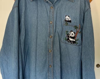 May include: Light blue denim button-down shirt with long sleeves. Features an embroidered panda bear design on the chest pocket. The shirt has a classic collar and buttoned cuffs. The tag on the collar reads "WWF".