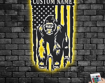 May include: A black metal silhouette of a gorilla standing in front of an American flag with the text "CUSTOM NAME" at the top. The silhouette is illuminated with yellow light.