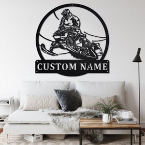 May include: Black metal wall art featuring a snowmobiler riding through a snowy landscape. The art is circular and includes the text "CUSTOM NAME" at the bottom.