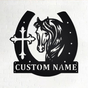 May include: Black metal horseshoe with a horse head silhouette and a cross design. The horseshoe has a personalized nameplate that reads "CUSTOM NAME".