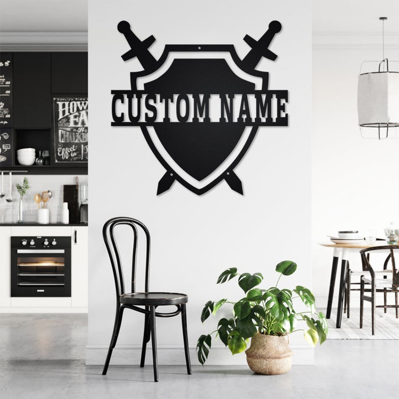 May include: Black metal wall decor featuring a shield with two swords crossed behind it. The shield has a white outline and the text "CUSTOM NAME" is written across the top.