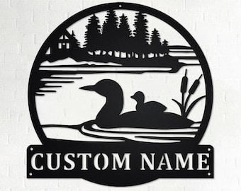 May include: Black metal silhouette of a loon and chick on a lake with a cabin and trees in the background. The text "CUSTOM NAME" is below the image.