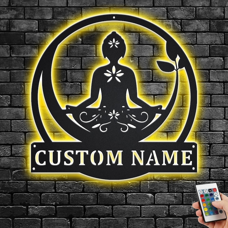 K&ouml;nnte beinhalten: Eine schwarze Wanddekoration aus Metall mit einer Silhouette einer Person, die in einem Kreis mit gelbem Schein meditiert. Die Worte "CUSTOM NAME" befinden sich am unteren Rand des Kreises.