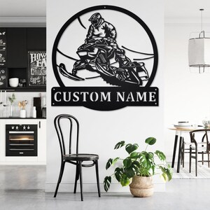 May include: Black metal wall art featuring a silhouette of a person riding a snowmobile. The art is circular and includes the text "CUSTOM NAME" at the bottom.