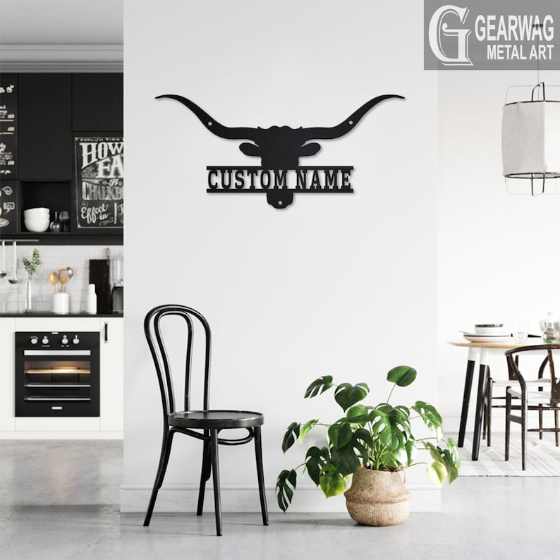 May include: Black metal wall art featuring a longhorn steer head silhouette with a personalized nameplate that reads "CUSTOM NAME". The art is mounted on a white wall in a modern kitchen setting.