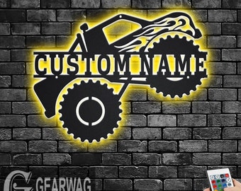 May include: Black metal silhouette of a monster truck with flames, with the words "CUSTOM NAME" in the centre. The truck is illuminated with yellow LED lights.