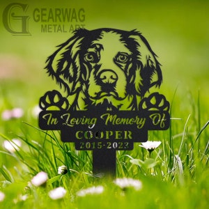 以下が含まれることがあります： 犬のシルエット、テキスト「In Loving Memory Of」、名前「COOPER」、日付「2015-2023」が刻まれた黒い金属製のガーデンメモリアル。