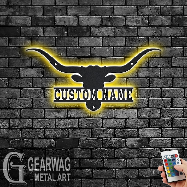 May include: Black metal silhouette of a longhorn steer head with large horns, illuminated with yellow light. The name "CUSTOM NAME" is displayed on a metal plaque below the steer head.