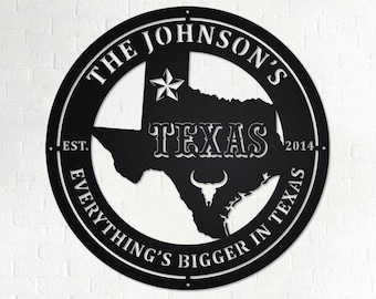 Könnte beinhalten: Schwarzes Metallschild mit einer weißen Umrandung des Bundesstaates Texas, einem Stern, einem Stierkopf und dem Text "The Johnson's Est. 2014 Everything's Bigger in Texas".