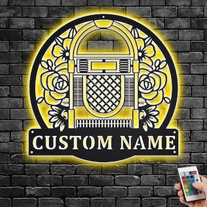May include: A black metal wall sign with a vintage jukebox design and floral accents. The sign is illuminated with yellow lights and has the text "CUSTOM NAME" at the bottom.