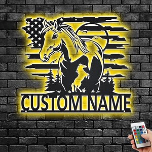 Könnte beinhalten: Schwarze Metallpferdesilhouette mit gelber Hintergrundbeleuchtung, vor einer Backsteinmauer. Das Design umfasst eine amerikanische Flagge, Bäume und den Text "CUSTOM NAME". Eine Fernbedienung befindet sich in der unteren rechten Ecke.