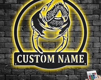 May include: A black metal wall sign with a cutout of a manatee and the text "CUSTOM NAME". The sign is illuminated with yellow LED lights and has a remote control.
