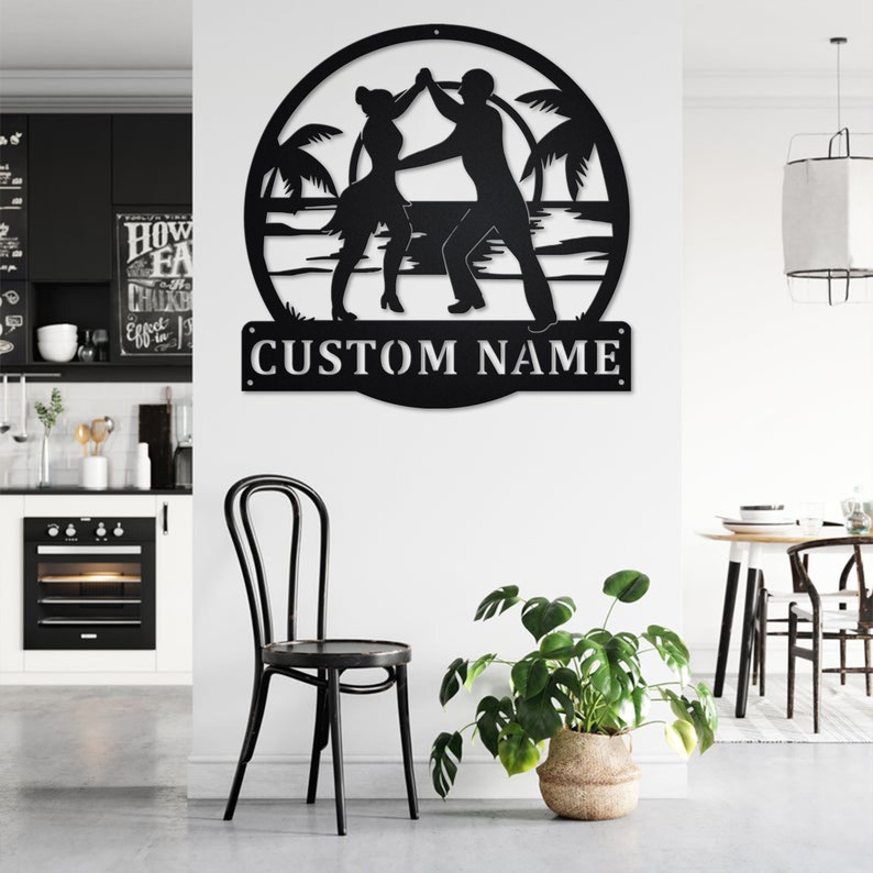 May include: Black metal silhouette of a couple dancing on a beach with palm trees. The silhouette is in a circle with the text "CUSTOM NAME" below it.