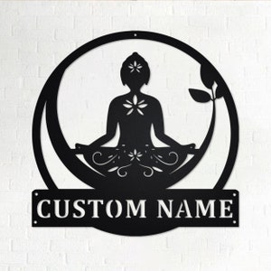 K&ouml;nnte beinhalten: Schwarze Wandkunst aus Metall mit einer stilisierten Silhouette einer Person in einer Yoga-Pose, umgeben von einem Kreis und floralen Designs. Die Kunst enth&auml;lt eine personalisierte Namensschilder mit dem Text "CUSTOM NAME".