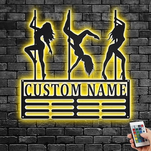 Könnte beinhalten: Schwarze Wanddekoration aus Metall mit drei Silhouetten von Frauen auf Stangen. Die Dekoration hat einen gelben Schein und der Text "CUSTOM NAME" befindet sich oben.