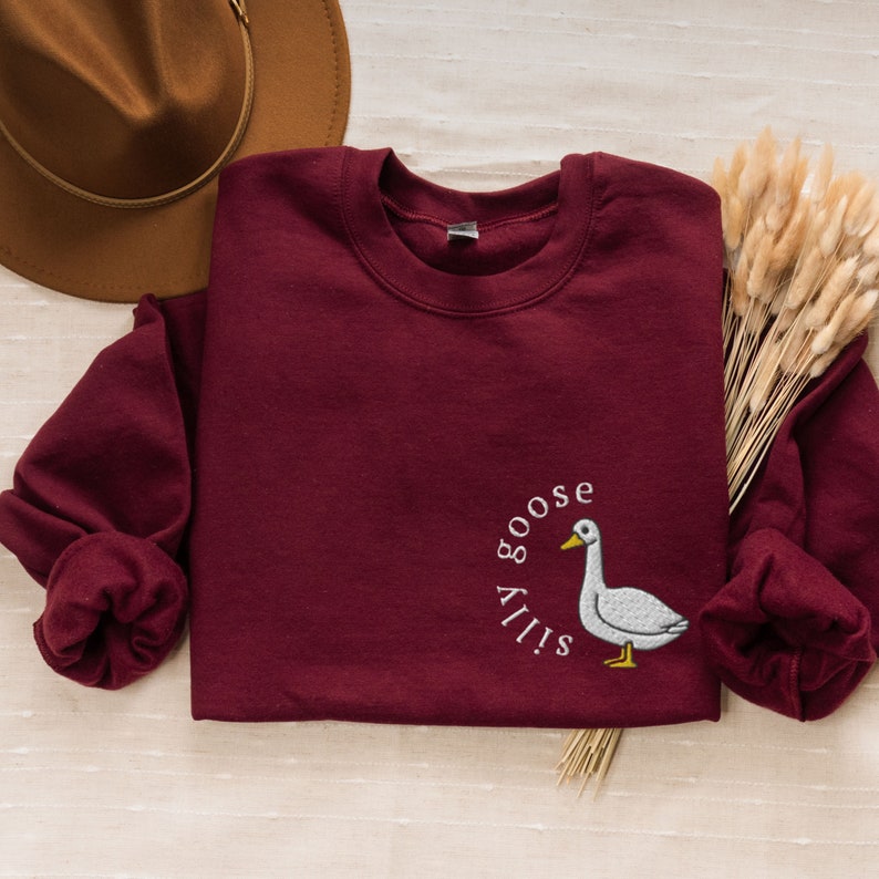 May include: A maroon sweatshirt with a white embroidered goose and the text "Silly Goose" on the front.