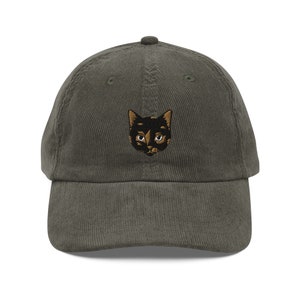 May include: A dark green corduroy baseball cap with an embroidered black cat face.
