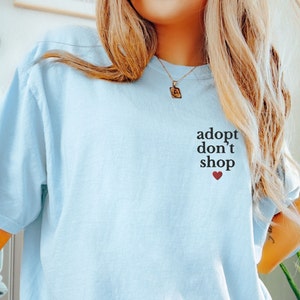 May include: A light blue t-shirt with the text "adopt don't shop" and a small red heart.