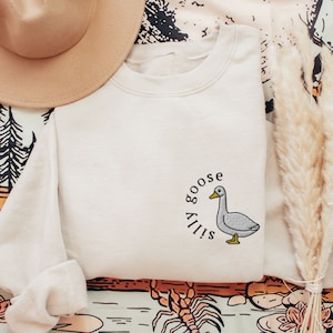 May include: A beige sweatshirt with a white goose and the text "Silly Goose" embroidered on the front.
