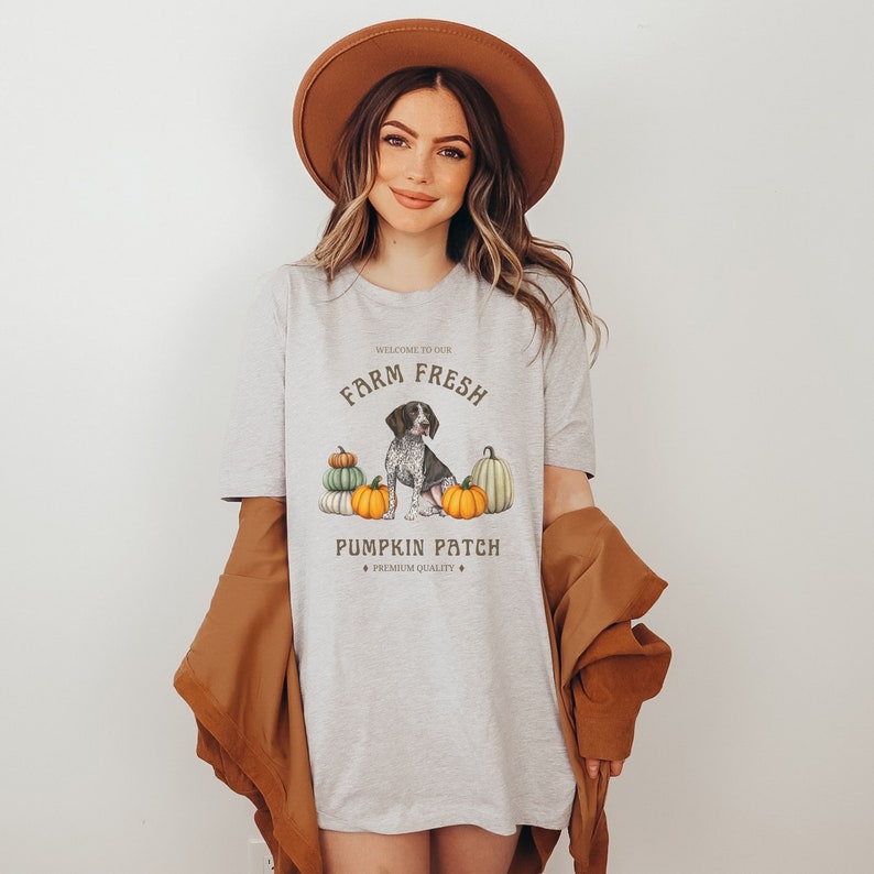 May include: A gray t-shirt with a graphic design of a dog sitting in front of pumpkins. The text on the shirt reads "Welcome to our Farm Fresh Pumpkin Patch - Premium Quality".