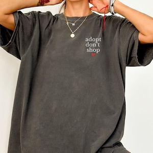 May include: A dark gray t-shirt with the text "adopt don't shop" and a small red heart.