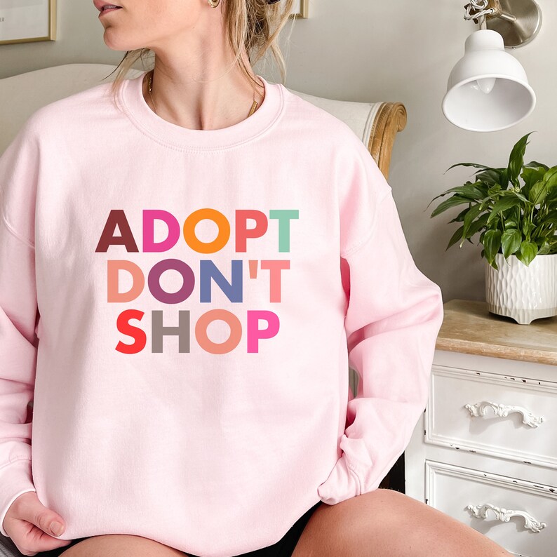 May include: Pink sweatshirt with the text "ADOPT DON'T SHOP" in colorful letters.