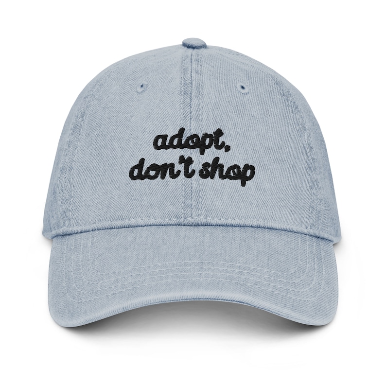 May include: A light blue denim baseball cap with black embroidered text that reads "adopt, don't shop".