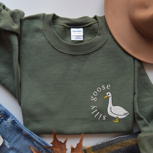 May include: A green sweatshirt with a white embroidered goose and the text "Silly Goose" in a circle around it.