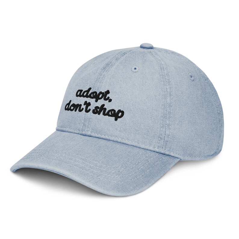 May include: A light blue denim baseball cap with black embroidered text that reads "adopt, don't shop".