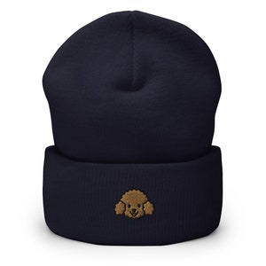 Puede incluir: Un gorro azul marino con una cara de caniche bordada en marr&oacute;n en la parte delantera.