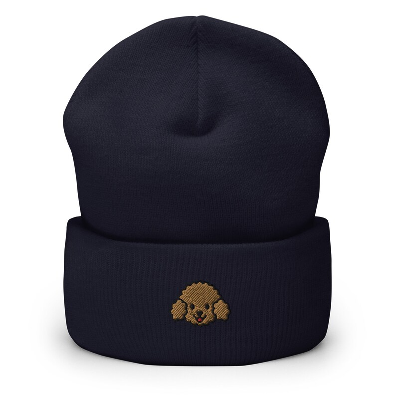 Puede incluir: Un gorro azul marino con una cara de caniche bordada en marr&oacute;n en la parte delantera.