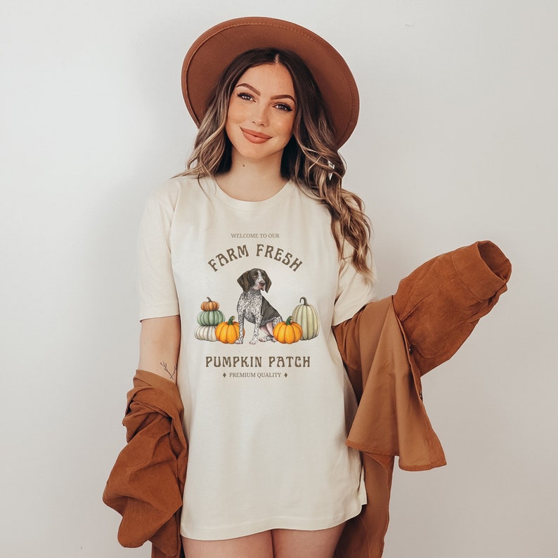 May include: A white t-shirt with a brown and white dog sitting in front of pumpkins. The text on the shirt reads "Welcome to our Farm Fresh Pumpkin Patch * Premium Quality *"