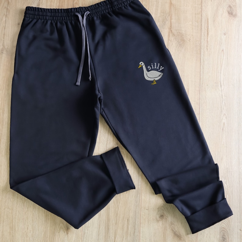 May include: Dark blue sweatpants with a white goose and the word "silly" embroidered on the right leg.